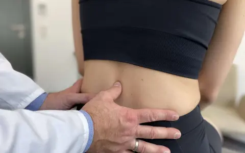 Lekarz bada odcinek lędźwiowy kręgosłupa pacjentki, oceniając objawy spondylozy lędźwiowej.