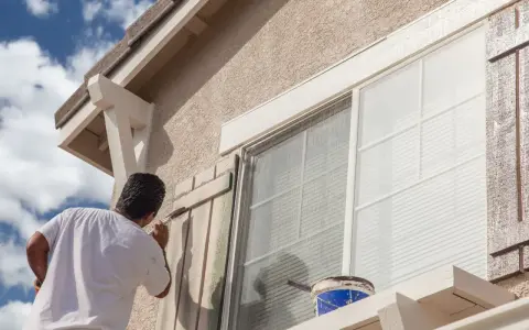 Un hombre pinta las contraventanas de una casa. El trabajo de pintar casas por fuera es esencial para su mantenimiento.