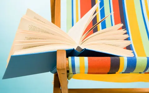 Un libro aperto, pieno di classici della letteratura, appoggiato su una sdraio a righe colorate.