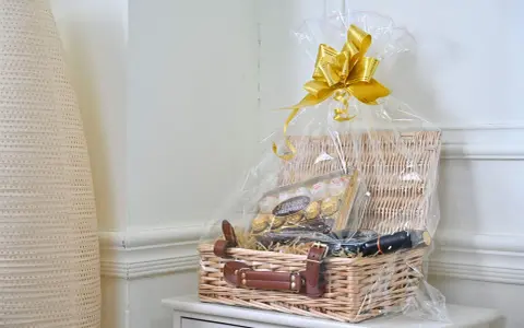 En vacker presentkorg med Ferrero Rocher-choklad och en flaska vin, inslagen i cellofan med en gyllene rosett.