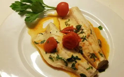 Filetti di branzino in padella con pomodorini e prezzemolo, un piatto leggero e saporito.