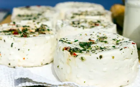 Kilka okrągłych serów labneh z ziołami i przyprawami na białej serwetce.