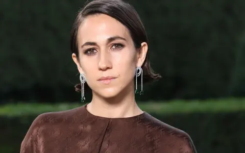 Delfina Delettrez Fendi indossa orecchini pendenti con diamanti e smeraldi, abbinati a un abito marrone con logo Fendi.