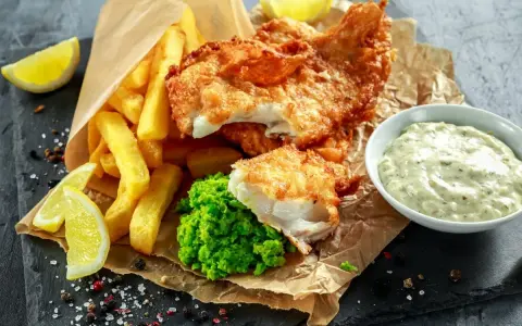 Poisson pané croustillant, frites dorées, purée de petits pois et une sauce tartare crémeuse pour accompagner ce plat de fish and chips.
