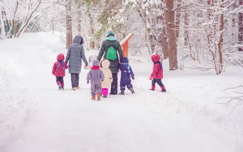 Kindergarten-Pflicht: Eine Gruppe Kinder und Erzieherinnen stapfen durch tiefen Schnee im Wald.