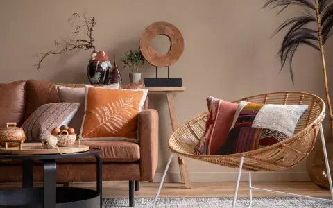 Un salon cosy avec un canapé en cuir marron, des coussins aux motifs ethniques et une chaise en rotin.