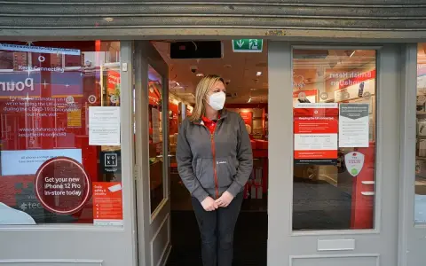 Kobieta w maseczce stoi przed zamkniętym sklepem Vodafone. Informacja na drzwiach głosi, że sklep jest otwarty tylko na odbiór zamówień online, nawet w bank holiday.
