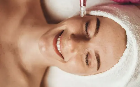 Uśmiechnięta kobieta poddana zabiegowi dermapenem. Po zabiegu ważne jest odpowiednie nawilżenie, dlatego warto wybrać łagodny krem po dermapenie.