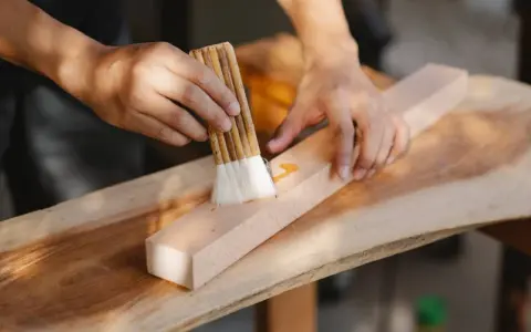 Un artisan ébéniste applique une finition sur un morceau de bois avec un pinceau.