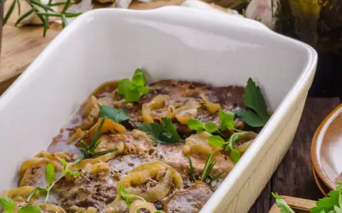 Schab pieczony w piekarniku w naczyniu, duszony z cebulą i ziołami. Aromatyczne danie gotowe do podania.