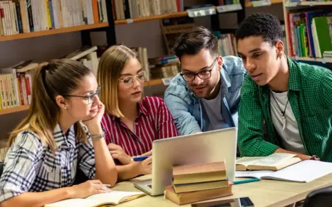 Studenci pochłonięci nauką historii przy laptopie w bibliotece.