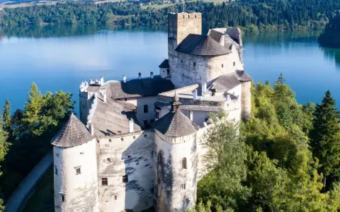 Zamek Dunajec, majestatyczna twierdza na skale, otoczona zielenią i błękitną wodą jeziora.