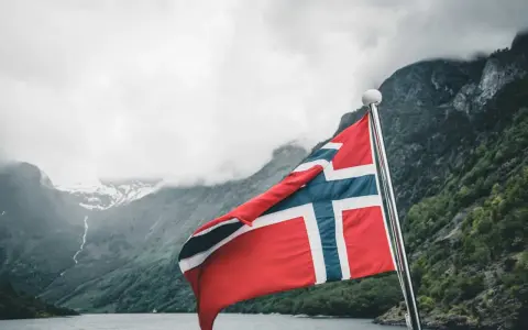 Norweska flaga na tle fiordu. Marzenia o wysokich zarobkach w Norwegii stają się rzeczywistością.