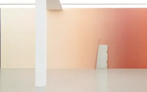 A gallery wall features a stunning gradient in art, transitioning from soft peach to warm coral. A rough stone slab leans against it.