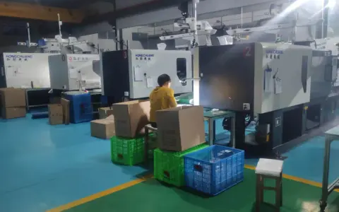 A person in a yellow jacket works at a station with boxes and crates, surrounded by injection molding machines, indicating low volume production.