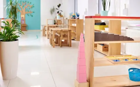 Un aula Montessori 0-3 años con mesas bajas, estanterías de madera y materiales didácticos como la torre rosa.