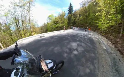 Motocyklista pokonuje krętą drogę stu zakrętów, otoczoną zielonym lasem.