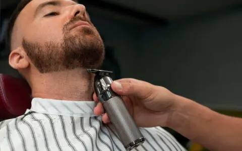Barbero perfilando la barba ancla de un cliente con una recortadora.
