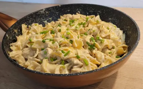 Tagliatelle z kurczakiem w sosie śmietanowym, posypane szczypiorkiem, podane w patelni. Pyszne danie gotowe do spożycia.
