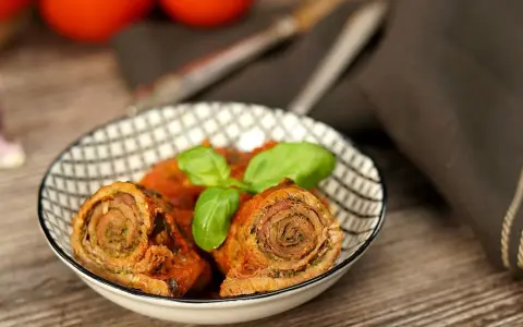 Zwei herzhafte involtini originalrezept in Tomatensoße, garniert mit Basilikum, in einer Schale auf Holztisch.