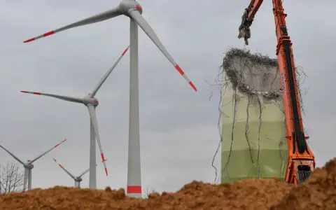 Abrissbagger demontiert eine Windkraftanlage. Im Hintergrund stehen noch weitere Windräder, die ihre lange Laufzeit hinter sich haben.