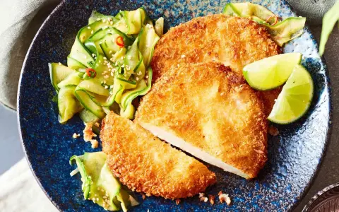 Knuspriges Kohlrabi-Schnitzel mit Gurkensalat und Limettenspalten auf blauem Teller.