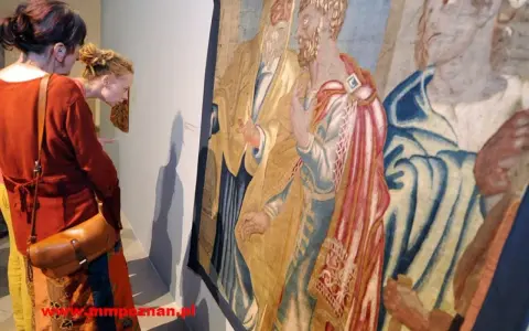 Dwie kobiety oglądają zabytkowy gobelin, przypominający stylem wyczółkowski obrazy. Detale postaci i bogactwo tkaniny przyciągają wzrok.