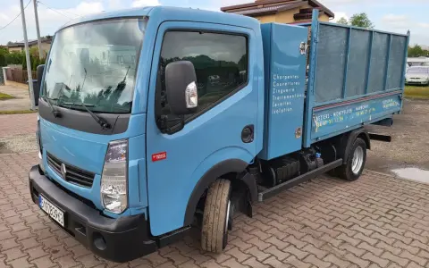 Niebieska ciężarówka Renault Maxity z otwartą skrzynią ładunkową, zaparkowana na brukowanym podjeździe.