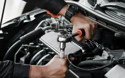 Mechanik wykonuje wymiana pompy paliwa krok po kroku, używając klucza nasadowego do odkręcenia śrub w silniku samochodu.
