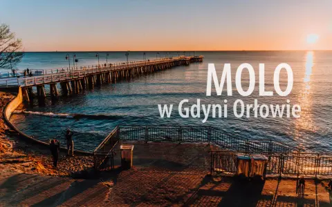Zachód słońca nad morzem, długie molo w Orłowie, ludzie spacerują po plaży.