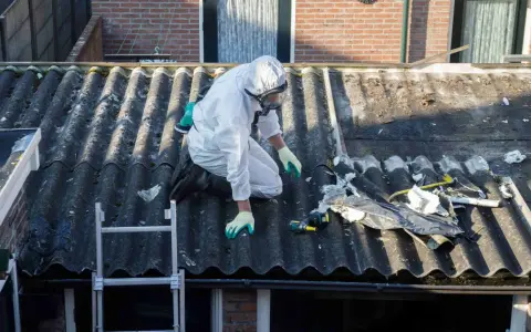 Travailleur en combinaison intégrale sur un toit en fibrociment, préparant le terrain pour une nouvelle peinture. Quelle peinture pour recouvrir peinture au plomb ?
