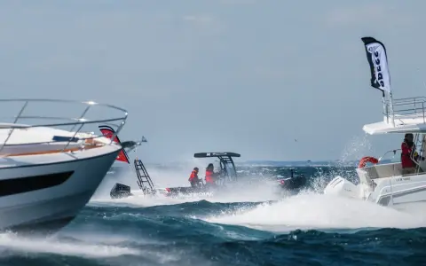 Trois bateaux en pleine navigation, éclaboussures d'eau, ciel bleu. L'un d'eux, un Zodiac, fend les vagues avec deux personnes à bord.