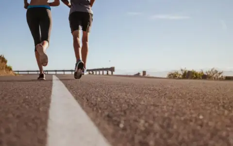 Coppia corre su strada asfaltata, godendosi la libertà e la velocità media corsa sotto un cielo azzurro.