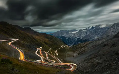 Ślady świateł samochodów wiją się serpentynami na stromych zboczach górskich, tworząc świetlisty szlak na przełęczy Stelvio.