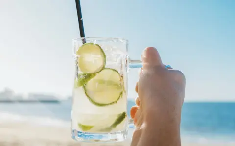 Orzeźwiająca Caipirinha czy Caipiroska z limonką i lodem w dłoni na tle plaży i morza. Idealny napój na upalny dzień.