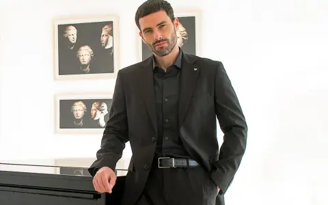 Uomo elegante in completo nero, camicia nera uomo abbinamento perfetto. Sfondo con quadri di busti classici.