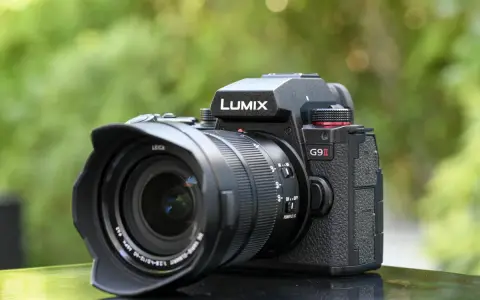Un appareil photo noir Lumix G9 II avec objectif Leica est posé sur une surface réfléchissante, avec un arrière-plan flou de verdure.