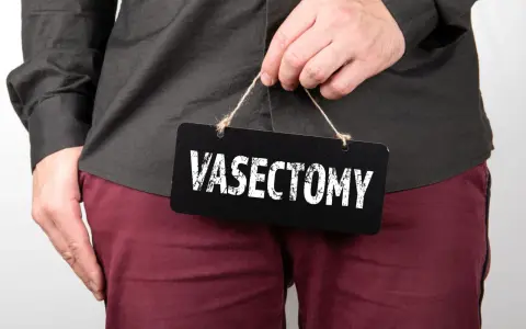 Mężczyzna trzyma tabliczkę z napisem "VASECTOMY". Czy po wazektomii można mieć dzieci? To pytanie nurtuje wielu.