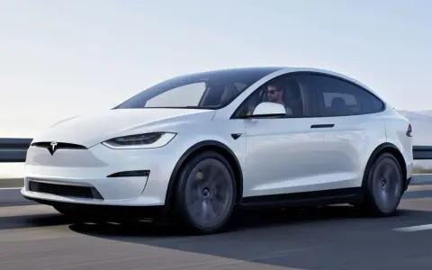 Biały Tesla X w ruchu, kierowca w okularach. Zastanawiasz się nad jego ceną?