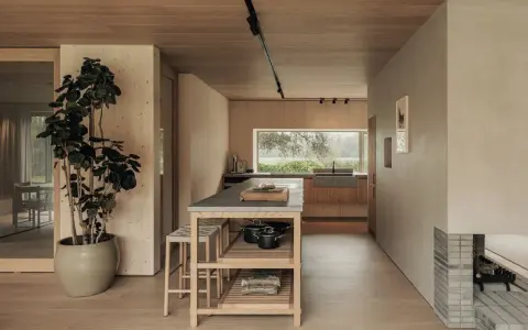 Un acogedor salón cocina pequeño con isla central, mucha madera y una gran ventana al exterior.