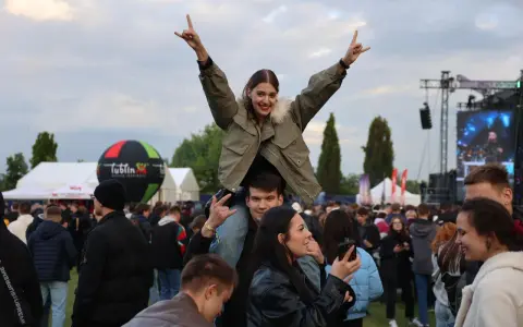 Dziewczyna na ramionach chłopaka cieszy się na Juwenaliach Politechniki Lubelskiej. W tle scena i tłum bawiących się studentów.