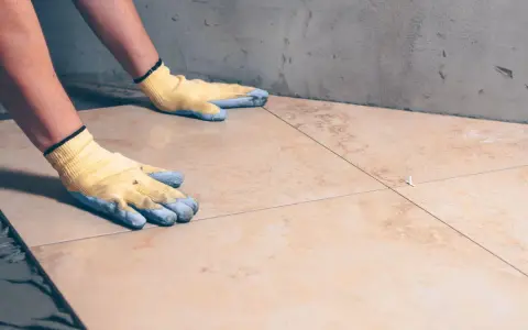 Pose de carrelage : mains gantées ajustant une nouvelle dalle sur la sous couche carrelage.