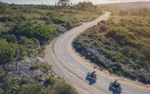 Due moto KTM sfrecciano su una strada tortuosa tra colline verdi. Un'avventura che celebra il KTM Connect.