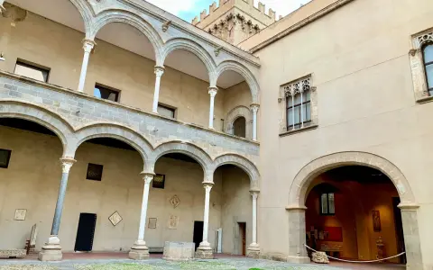 Cortile di Palazzo Abatellis, con arcate sovrapposte, finestre gotiche e opere d'arte esposte.