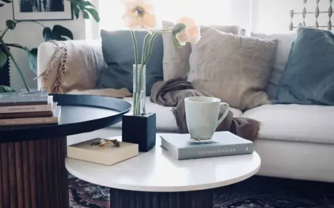 Ett stilrent soffbord med ribbad bas, perfekt för ditt hem. Här finns en bok, en mugg och en vas med blommor.