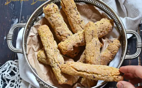 Biscotti senza farina dorati e croccanti, cosparsi di zucchero, in un cestino d'argento. Una mano ne prende uno.