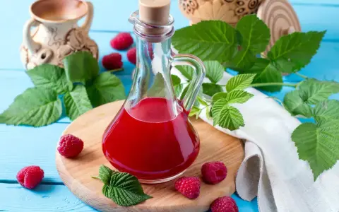 Malinowy ocet balsamiczny do sałatek, deserów, marynat. W butelce z korkiem, otoczony świeżymi malinami i liśćmi.