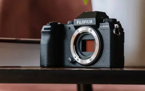 Czarny aparat Fujifilm X-S20 z obiektywem bez obiektywu, leżący na drewnianym stole obok książki.