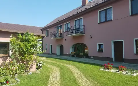 Urokliwe łowisko Trzeboszowice. Różowy budynek z balkonami, zielony ogród i ścieżka z kostki brukowej.