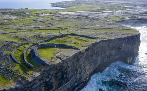 Steile Klippen und alte Steinmauern auf einer grünen Insel vor Galway, Irland. Wellen schlagen gegen die Felsen.